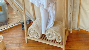 Un porte-vêtements en bois sur lequel sont suspendues deux robes blanches, et une serviette enroulée qui se trouve sur le sol.