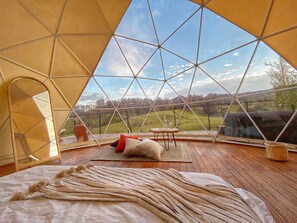 A cozy room with a large window, wooden flooring, and a bed with a striped blanket. - Bohemia Glamping (La Unión de Sucre)