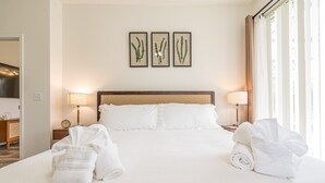Una camera d'albergo con un letto grande, due abat-jour, una sveglia e tre stampe botaniche incorniciate appese al muro.