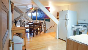 Une cuisine avec un plancher en bois, une table à manger avec des chaises, un réfrigérateur et un four.