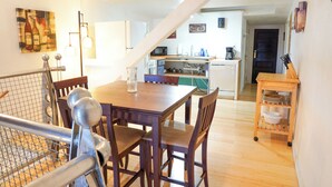 Un coin repas avec une table et des chaises en bois, une cuisine à l’arrière-plan et un escalier menant à un autre niveau.