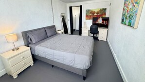Une chambre à coucher avec un lit, un bureau, une chaise, un téléviseur et un tableau accroché au mur.