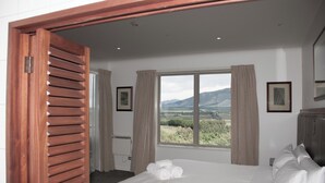 Quarto de hotel com uma cama grande, janela com vista para as montanhas e porta de madeira.