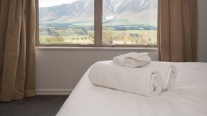 Quarto de hotel com cama, janela com cortinas e vista para montanhas.