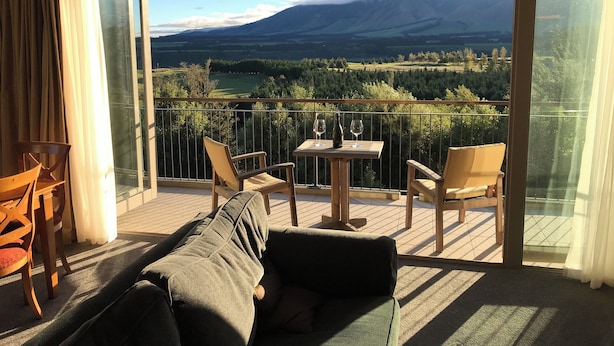 Uma varanda com um sofá, cadeiras e uma mesa com copos de vinho e uma garrafa.