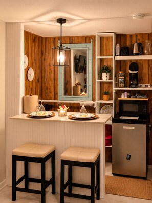 A kitchen with wooden paneling, a built-in microwave, and a refrigerator. There are two stools and a small table with plates and candles. - Rural • Private MasteRoom • Pets Friendly • Free Parking (Hawthorne)