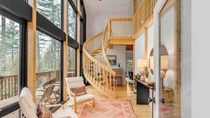 Une pièce spacieuse avec une grande fenêtre, un escalier en bois et un coin salon confortable.