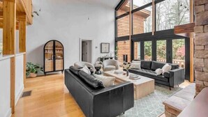 Un vaste espace de vie avec une grande fenêtre, un canapé noir, une table basse et un meuble en bois.