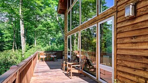 Une terrasse en bois avec des meubles d’extérieur, de grandes fenêtres et une vue sur une forêt.