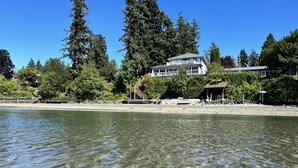 A waterfront property with a large house, a wooden deck, and a stone pathway leading to a dock.