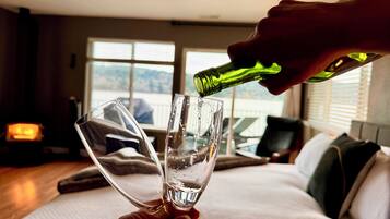 Een hand schenkt water in een glas op een bed in een kamer met een groot raam en een open haard.