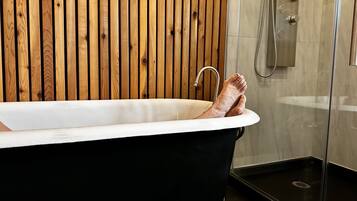 A bathtub with a wooden panel wall, a shower area, and a tiled floor.