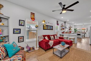 A modern living room with a red sofa, a coffee table, and a floor lamp. There is a kitchen area with a dining table and chairs visible in the background.