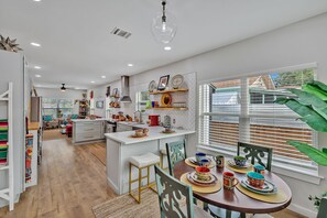 A modern kitchen with a central island, wooden flooring, and a dining area with colorful tableware.