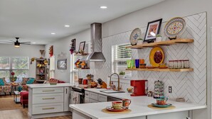 A modern kitchen with white cabinetry, a central island, and decorative plates on shelves. - Coco House rental home sleeps 6, ample outdoor seating, jacuzzi and a golf cart! (San Antonio)