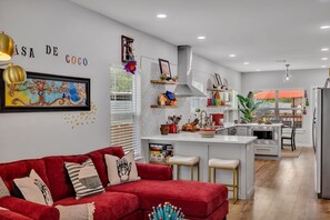 A modern kitchen with white countertops, a red sofa, and a dining area with a red umbrella.