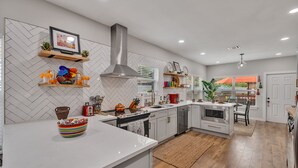 A modern kitchen with white cabinetry, a herringbone-patterned backsplash, and a central island with a colorful bowl. - Coco House rental home sleeps 6, ample outdoor seating, jacuzzi and a golf cart! (San Antonio)