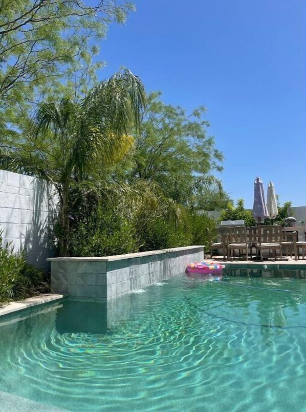 Relax by the serene pool surrounded by lush greenery and lounge chairs.