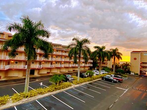 A multi-story hotel with balconies, a parking lot, and palm trees.