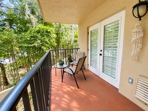 A balcony with a table and chairs, a potted plant, and a decorative wall hanging.