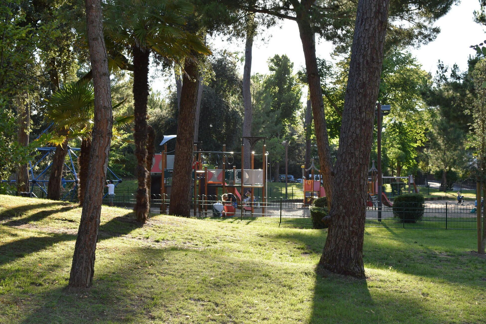 Ein Park mit Spielgeräten, Bäumen und einem eingezäunten Bereich.