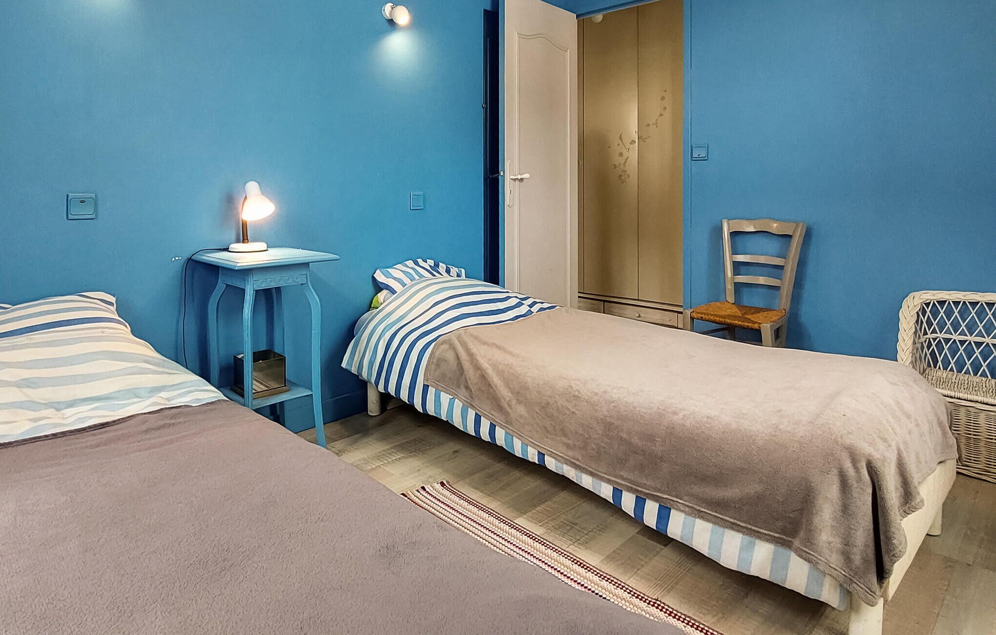 Une chambre avec deux lits, une table de chevet avec une lampe, une chaise et une armoire.