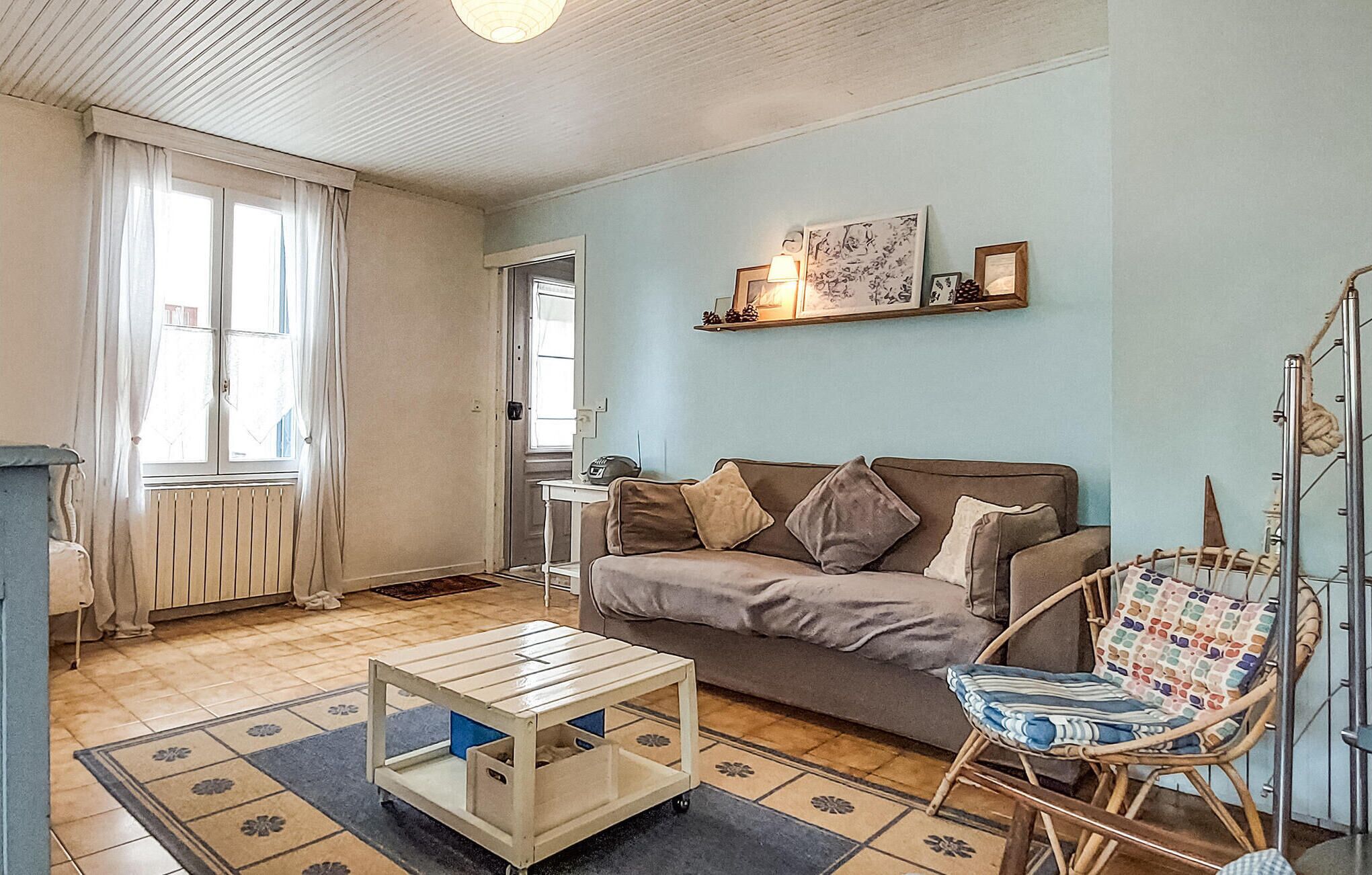Un salon comprenant un canapé, une table basse, un fauteuil, un radiateur, une porte et une étagère murale ornée de tableaux.