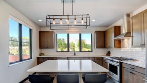 A modern kitchen with a large island, bar stools, a stove, and a view of the outdoors. - Downtown WP Loft 21 I Rooftop Hot Tub & Lounge I Great Views I Bunks I Discounted Attractions (Winter Park)