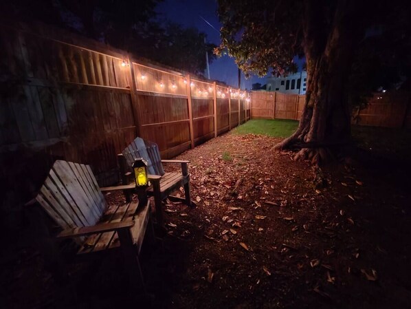 A wooden deck with a bench and a lantern, surrounded by a wooden fence and string lights.
