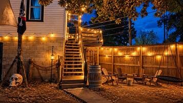 Ein Garten mit einer Holzterrasse, einer Leiter zu einem überdachten Bereich und Lichterketten.