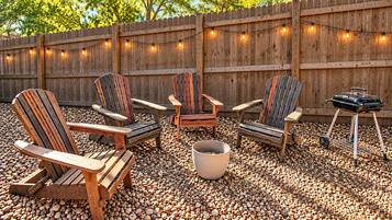 Un espace extérieur aménagé avec des chaises Adirondack, un barbecue et des guirlandes lumineuses.