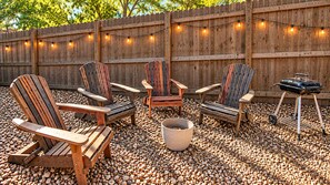 Un área de estar al aire libre con sillas Adirondack, una parrilla y luces colgantes.