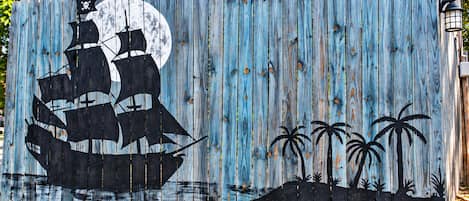 Una cerca de madera con un barco pirata y palmeras pintados.