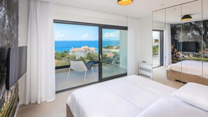 Ein modernes Hotelzimmer mit einem großen Bett, einem Balkon mit Meerblick und einem Flachbildfernseher.