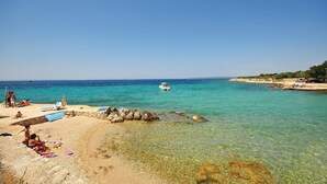 Ein Strand mit klarem türkisblauem Wasser, einer felsigen Küste und einigen Sonnenanbetern.