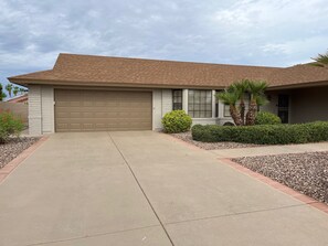 A single-story house with a garage, a driveway, and a well-maintained front yard with landscaping. - Your Private 19th Hole With Golf Cart Included In Rental (Sun City West)