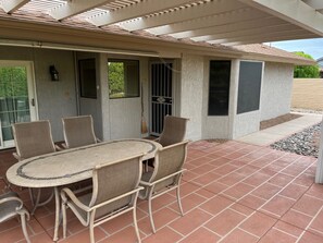 An outdoor patio with a round table and six chairs, a covered area with a roof, and a door with a window. - Your Private 19th Hole With Golf Cart Included In Rental (Sun City West)