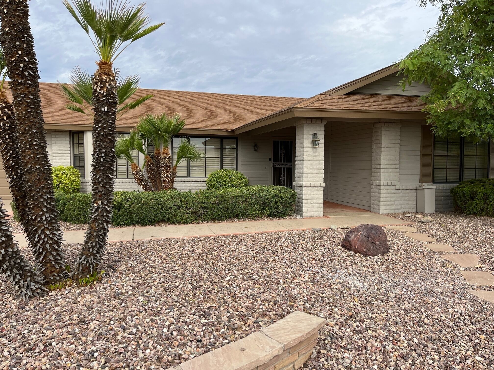 A building with a tiled roof, stone pillars, and a gravel driveway.