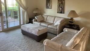 A living room with a sofa, ottoman, two lamps, and artwork on the wall. - Your Private 19th Hole With Golf Cart Included In Rental (Sun City West)