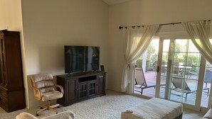 A living room with a flat-screen TV, a dark entertainment unit, and a large window with curtains. - Your Private 19th Hole With Golf Cart Included In Rental (Sun City West)