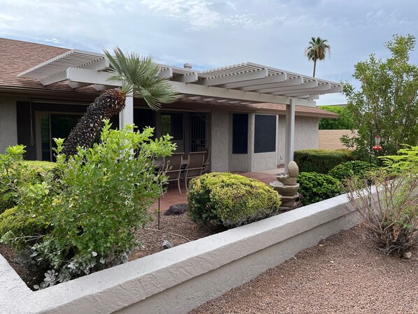 A house with a covered patio, a palm tree, and a well-maintained garden.