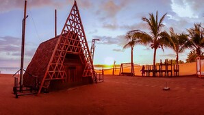 A beach hut with a thatched roof, surrounded by palm trees and a sandy beach. - Baos Hotel & Restaurant (Aticama)