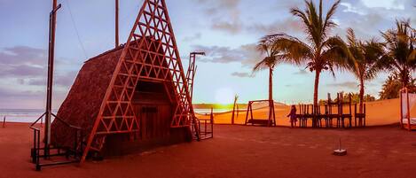Uma cabana de praia com telhado de palha, rodeada por palmeiras e uma praia de areia.