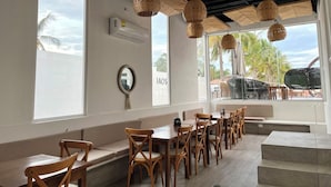 A restaurant with wooden tables and chairs, large windows with a view of palm trees, and woven ceiling lamps. - Baos Hotel & Restaurant (Aticama)