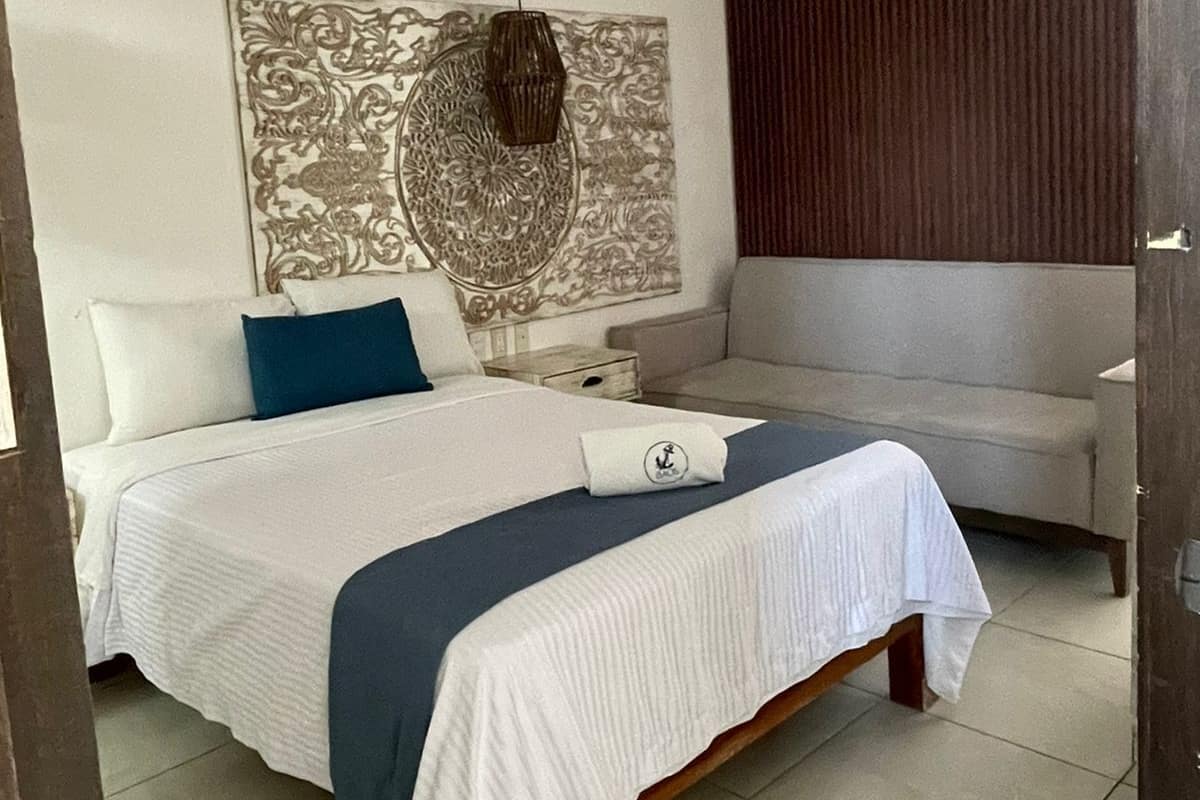 A hotel room with a large bed, a wooden nightstand, a white sofa, and a decorative wall panel.