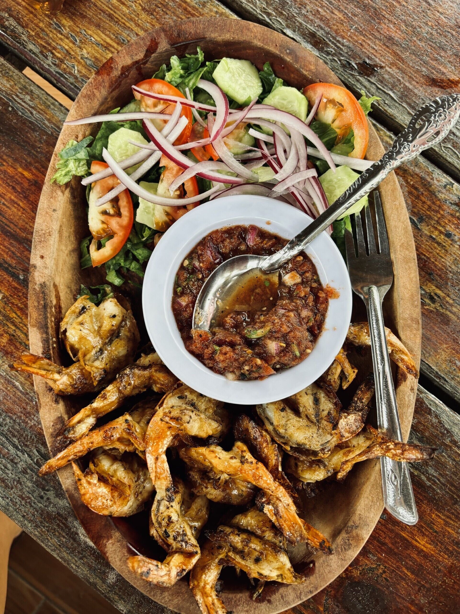 Un plateau de service en bois contenant des ailes de poulet grillées, une salade et un bol de sauce.