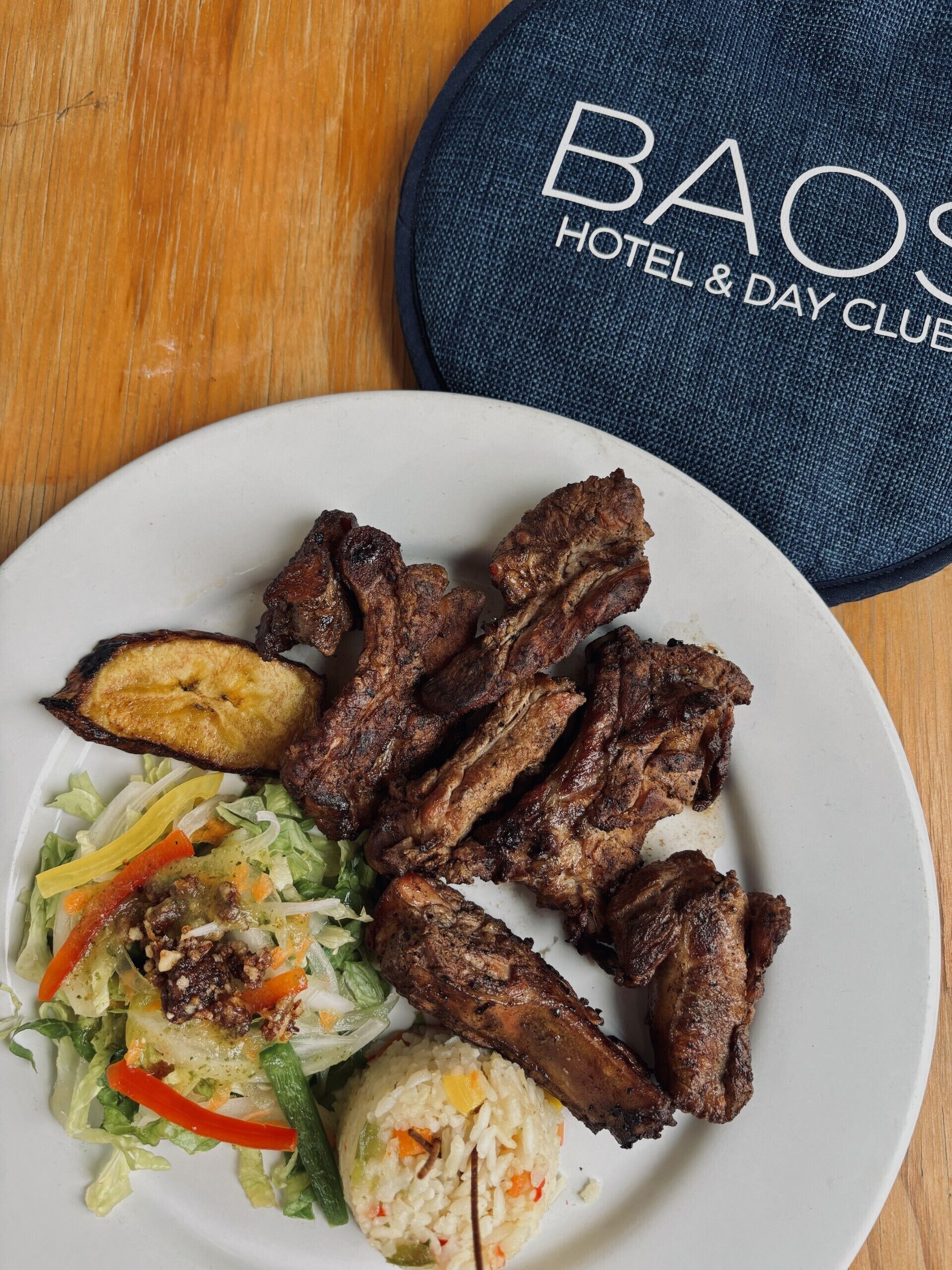 A plate of grilled meat, fried plantains, and a salad with rice.