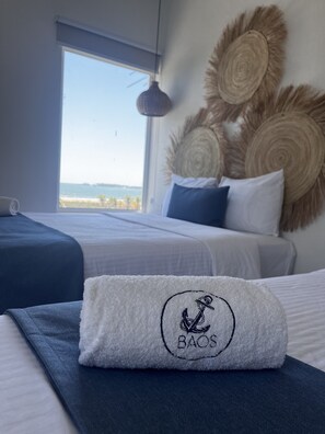 A hotel room with a bed, a window with a view, and a towel with a logo. - Baos Hotel & Restaurant (Aticama)