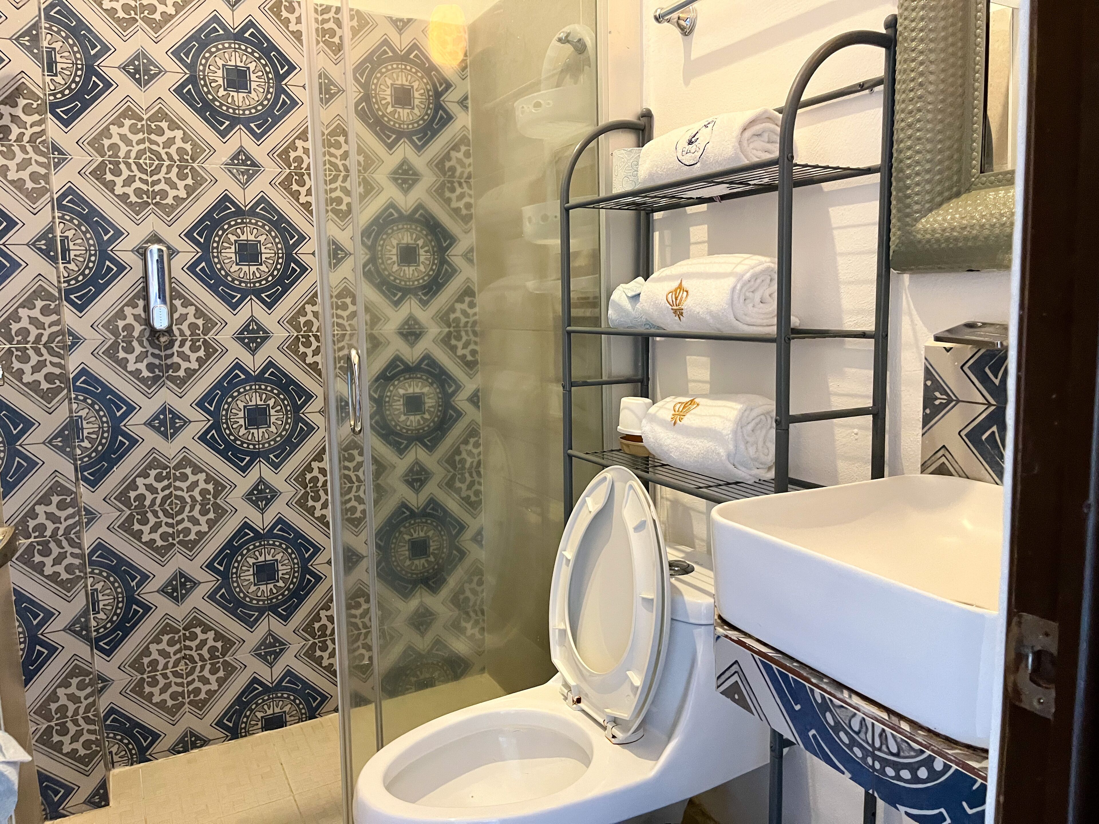A bathroom with patterned tiles, a toilet, a sink, and a towel rack with neatly folded towels.