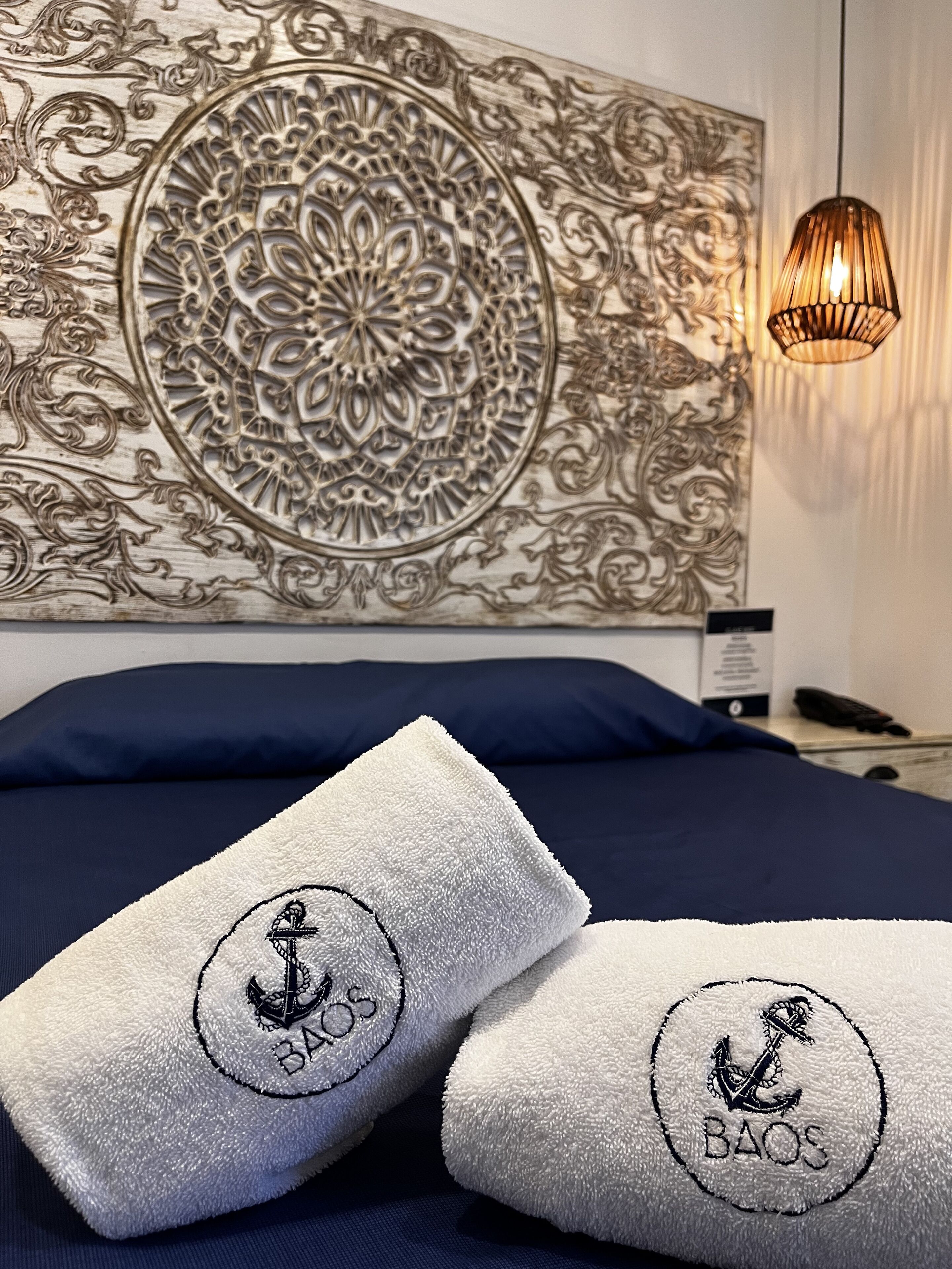 Una cama con ropa de cama azul marino y dos toallas blancas con el bordado 'BAOS'.